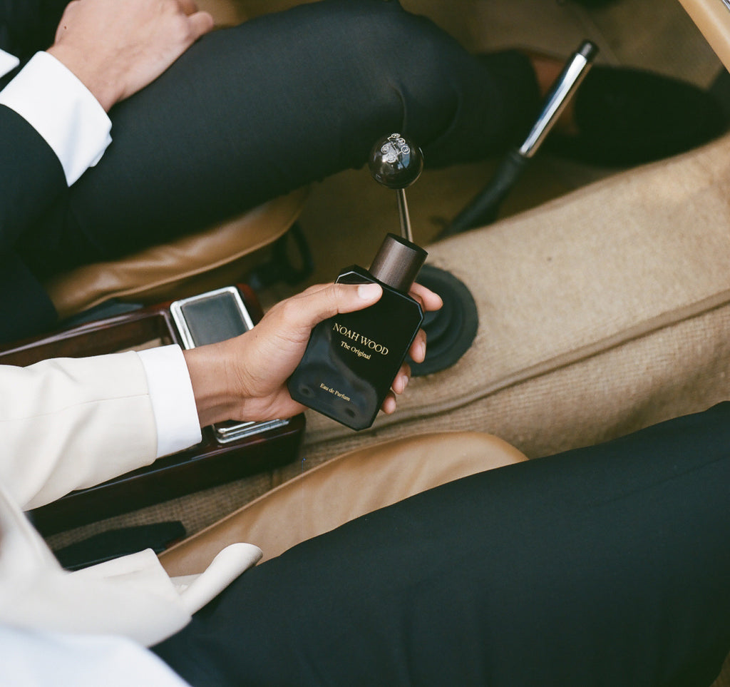 Person holding a black perfume bottle with a car interior in the background